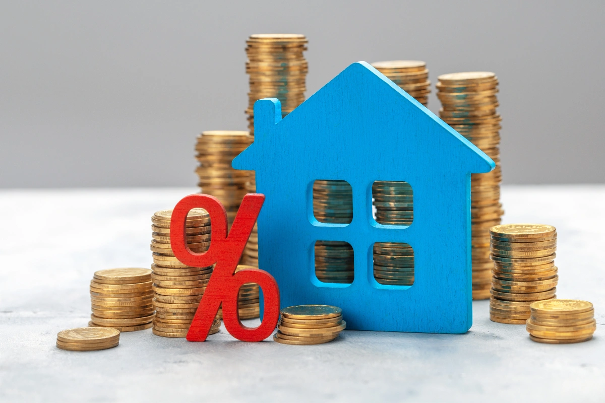 Blue house icon and red percent sign on stacks of coins symbolizing changing mortgage interest rates and home loan costs.