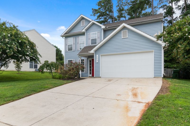 Charming two-story suburban house with a spacious driveway surrounded by green trees and shrubs.