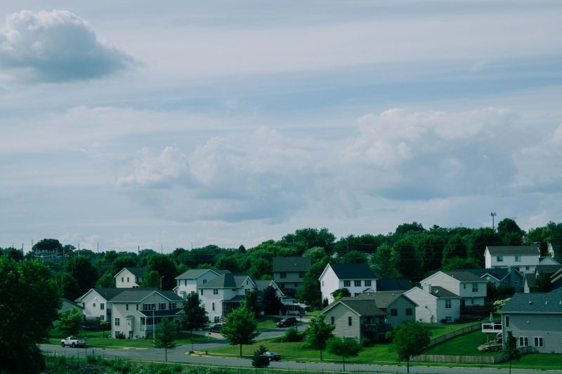 Picturesque suburban houses with well-maintained lawns under a blue sky dotted with clouds.