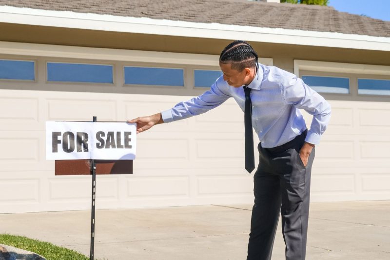 A real estate agent placing a for sale sign outside a suburban house.